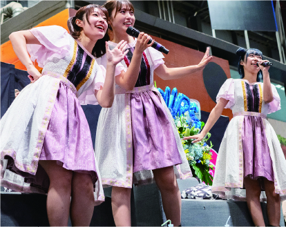 ピンクのワンピースを着用したアイドルが3人でプロモーションを行う様子